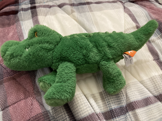 Fuzzy green gator plush on a bed