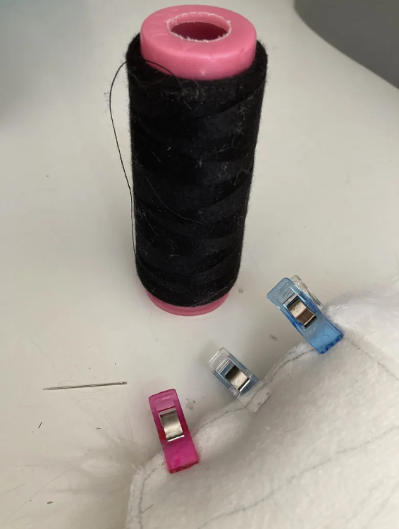 Black thread, needle, and two pieces of fur attatched with sewing clips