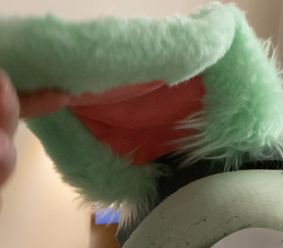 Green floppy fursuit ear with longer fur near the base and shorter fur everywhere else