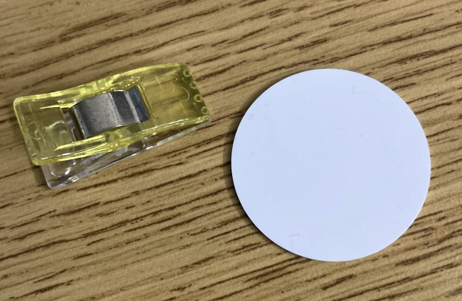 A white circular NFC tag, next to a sewing clip for scale