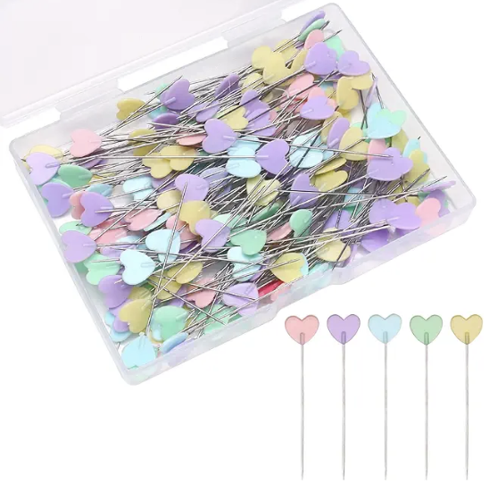 A container of pins with heart-shaped pinheads. They are in assorted pastel colors.