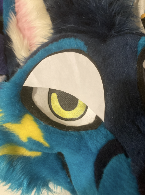 Paper template on a teal folf fursuit head's eye, making him look angry